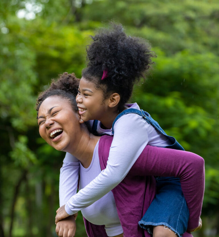 Woman carrying a young girl on her back laughing
