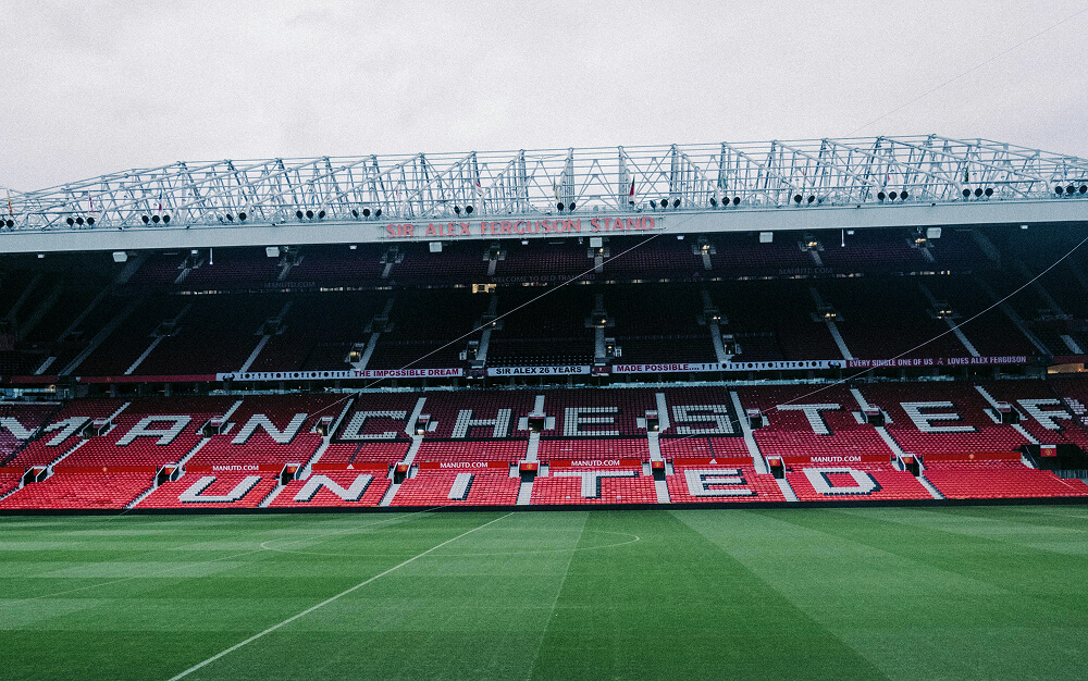 Manchester United football stadium. The football pitch and empty red stadium seating